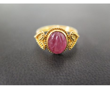 An unusual 22 carat gold ring set with a carved cabachon pink stone, believed to be tourmaline, in a collet setting, flanked 