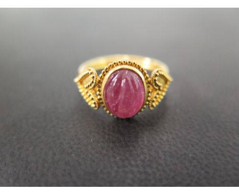 An unusual 22 carat gold ring set with a carved cabachon pink stone, believed to be tourmaline, in a collet setting, flanked 