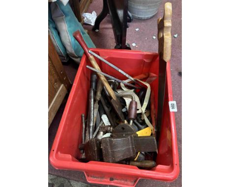 A red crate containing a quantity of assorted tools including an axe and a small bench vice