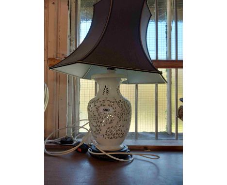 A white glazed ceramic table lamp of reticulated design, set on wooden stand