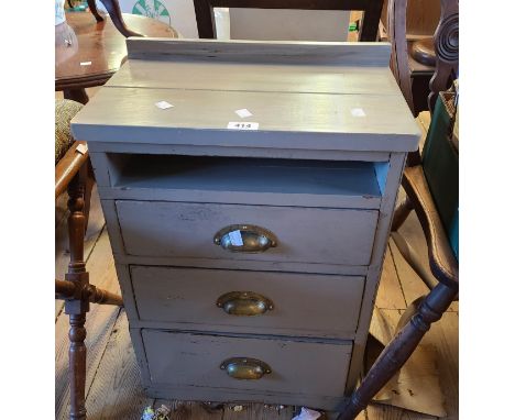 A grey painted wood three drawer bedside chest with brass cup handles
