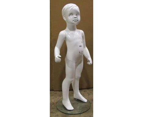 A shop window mannequin in the form of a child, with white glazed finish on a circular glass base, 80cm high 
