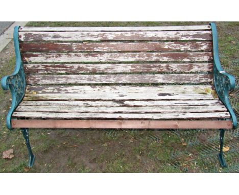 A two seat garden bench with weathered timber lathes, raised on decorative pieced cast iron end supports, with scrolling foli