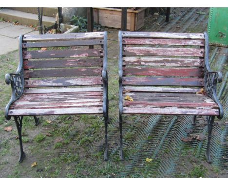 A pair of garden chairs with weathered timber lathes raised on decorative pierced cast iron supports, with scrolling foliate,