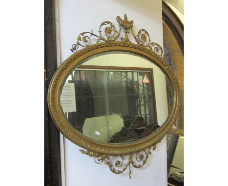 An oval overmantle mirror in the Adams style, the mirror with bevelled edge plate surmounted by an urn, flowers and scrolls, 