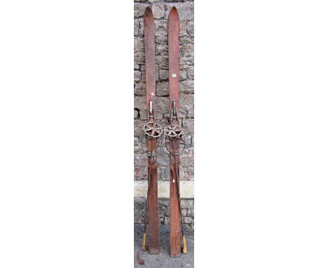 A pair of vintage wooden skis and poles with metal clips and fittings, and remains of an indistinct transfer printed label 