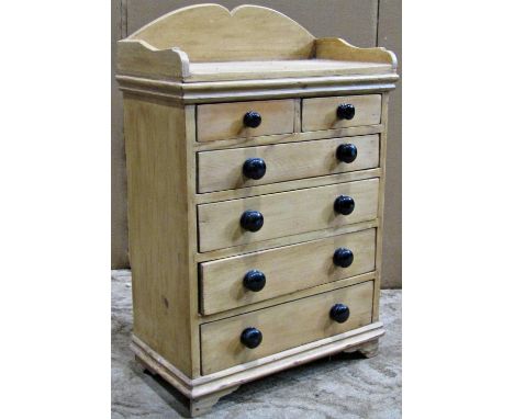 A small Victorian stripped and waxed pine miniature chest of four long and two short graduated drawers, with black ceramic kn