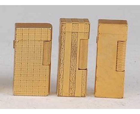 A collection of three Dunhill gilt metal pocket cigarette lighters, each having naturalistic engine turned decoration with hi