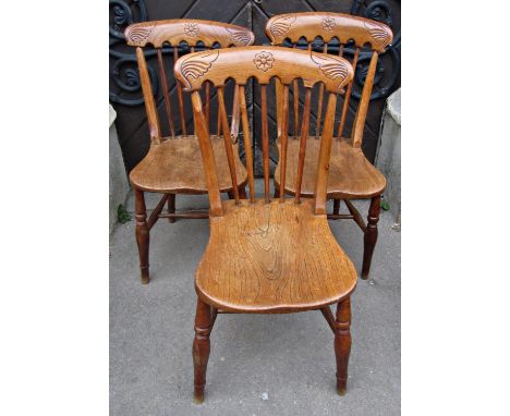 A set of three 19th century Windsor elm and beechwood stick back kitchen chairs with saddle shaped seats and carved cresting 