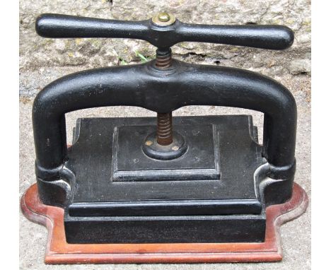 A vintage cast iron book press with central screw thread and mounted on a shaped timber board 34 cm high x 45 cm wide approxi