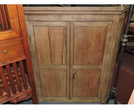 An early 19th century bleached oak hanging corner cabinet, the two doors enclosing a painted shaped shelf interior, W. 100cm.