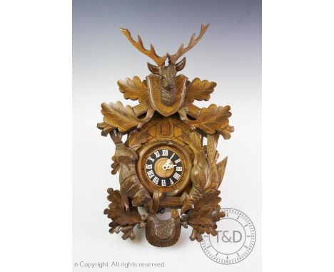 A mid 20th century West German carved oak cuckoo clock, the case applied with a carved stags mask, figure of a rabbit and the