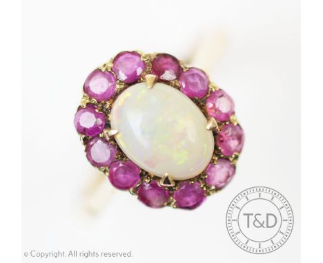 An opal and ruby cluster ring, London 1963, the central oval opal within a surround of twelve circular rubies, all set in 9ct