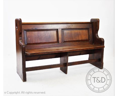 A Victorian pitch pine pew, having a twin panel back and rear book shelf above a board seat, raised upon shaped supports each