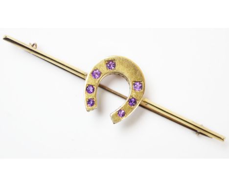 A 20th century amethyst set bar brooch, designed as a horse shoe with seven claw set amethysts, set in yellow metal stamped '