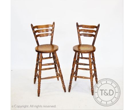 A set of four stained beech wood bar stools, each with a graduated ladder back, circular seat on turned legs (4) 