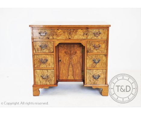 A George III style walnut knee hole desk, with an arrangement of seven drawers around a central cupboard door, on bracket fee