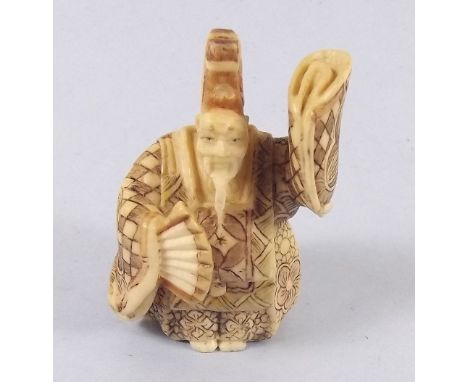 A Japanese ivory Meiji period netsuke of a ceremonial figure with elaborate costume and fan - signed