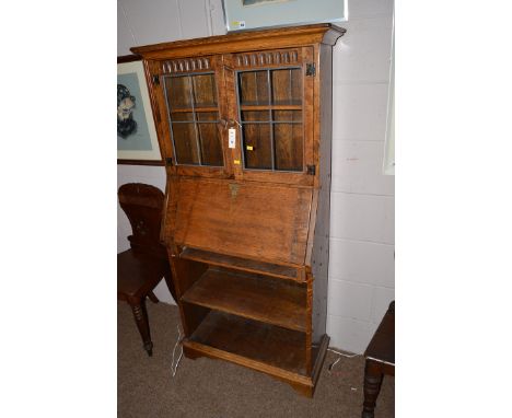 A reproduction carved and stained oak small bureau bookcase with flared cornice, two leaded glass panelled doors enclosing sh