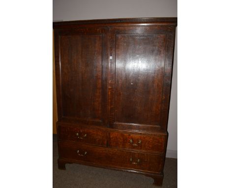 A Georgian oak linen press, with flared dentil cornice above two rectangular panelled doors enclosing hanging space and a sin
