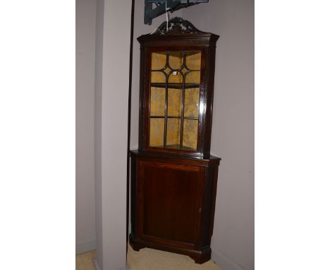 An early 20th Century mahogany corner display cabinet, the swan neck pediment of pierced floral form above blind fret frieze,