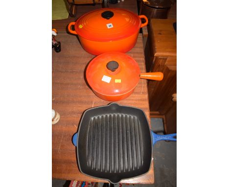 A large Le Creuset oval enamel casserole dish and cover; a similar pan and cover; and a blue Le Creuset griddle pan.