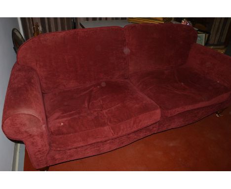 A sofa upholstered in red coloured dralon, with loose back and seat cushions, raised on turned legs terminating in brass and 