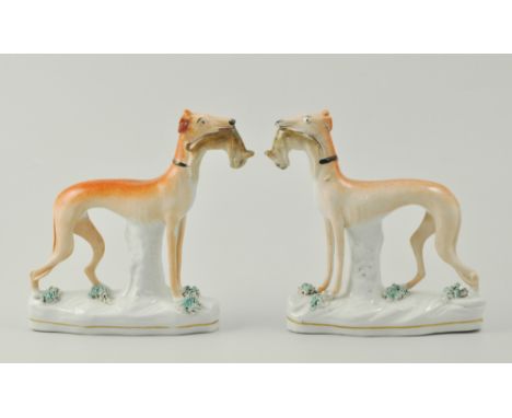 Pair of Staffordshire greyhounds, each model standing holding hares, raised on gilt-lined bases, height 16cms. 