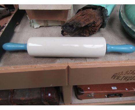 A white ceramic rolling pin with blue wooden handles 