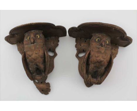 A PAIR OF LATE 19TH CENTURY BLACK FOREST CARVED WOOD WALL BRACKETS, owls perched on oak branches with leaves, inset glass eye