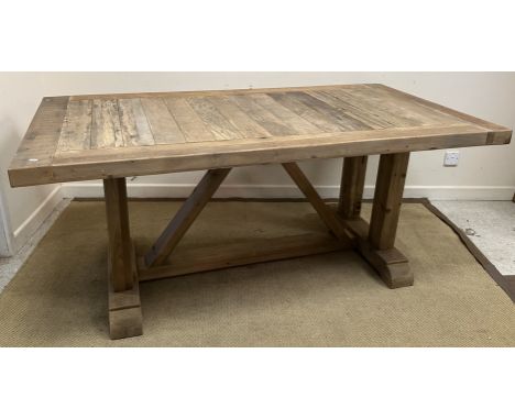 A driftwood type plank top dining table, the top with cleated ends and sides on twin pillar end supports united by a hay rake