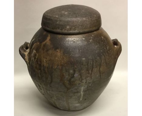 A large ovoid shaped smoke-fired lidded stoneware pottery vessel with green glaze interior and lug handles. Apparently unmark