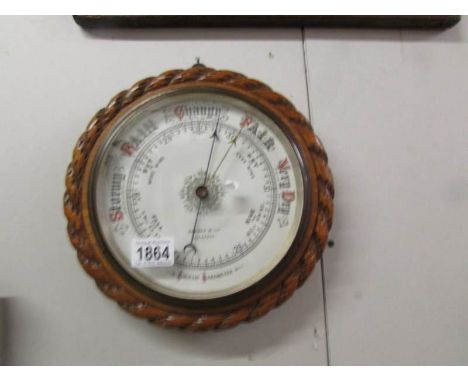An Edwardian oak barometer with pie crust edge and porcelain face by Symons & Son, Lancaster.