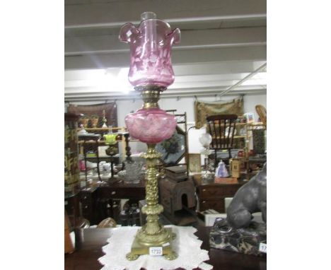 A brass oil lamp with cranberry font and shade.