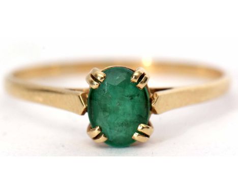 Yellow metal emerald ring, the oval faceted emerald 8x6mm, four claw set and raised between plain polished angular shoulders,