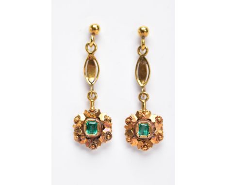 A PAIR OF YELLOW METAL, EMERALD SET DROP EARRINGS, each suspending an emerald cut emerald within a decorative floral surround