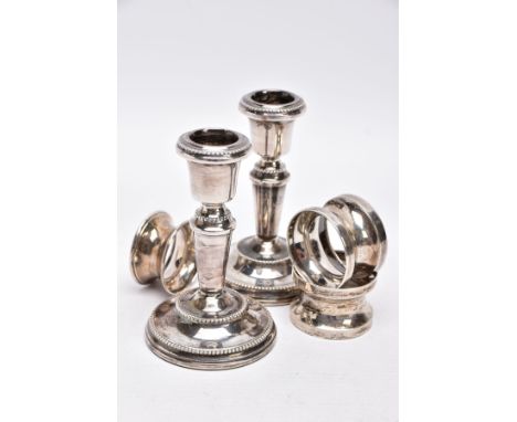 A PAIR OF SILVER DWARF CANDLESTICKS AND THREE NAPKIN RINGS, each candlestick has a round weighted base with a beaded rim, tap