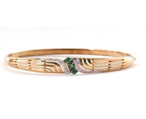 A 9ct emerald and diamond bangle, the hinged bangle set to centre with three small emeralds and an aysmetric tapered flourish