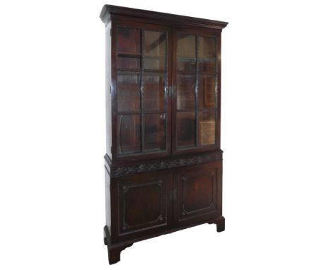 A late Georgian mahogany cupboard bookcase, the outswept pediment with dentil moulding over a pair of glazed doors enclosing 