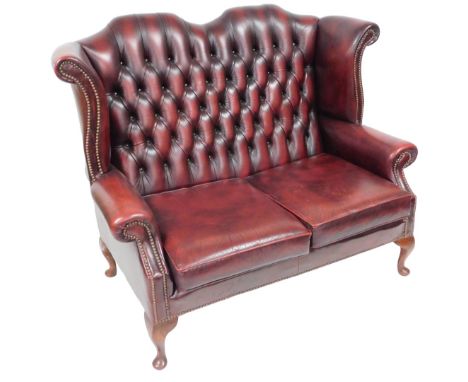 A Chesterfield oxblood red leather wingback two seater sofa, with button back and loose cushion seats, raised on cabriole leg