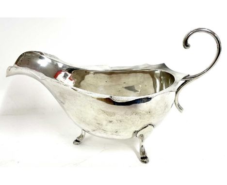 White metal sauce boat with card cut rim having a flying scroll leaf handle supported on three feet, stamped silver, 160 gms