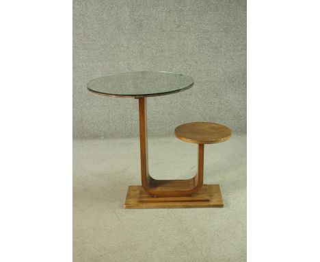 An Art Deco teak table and stool, with a circular glass table top, on a support which curves up to a circular seat, on a step