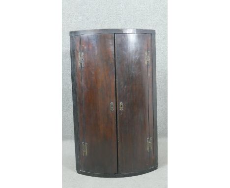 A George III mahogany bow front corner cabinet, with a pair of curved cupboard doors, enclosing shelves. H.94 W.55 D.37cm 