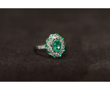 A PLATINUM EMERALD AND DIAMOND DRESS RING, set with a central oval-cut emerald, surrounded by diamonds and emeralds with diam