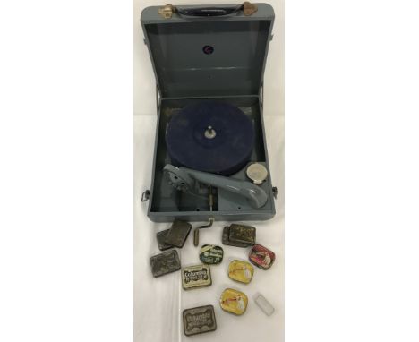 A vintage metal cased portable record player with a collection of needle tins. Tins include His Masters Voice and Columbia. 