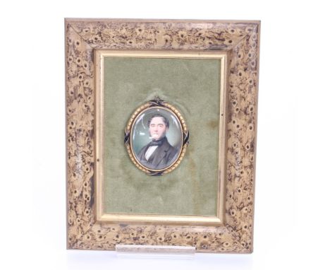 A 19th century oval portrait miniature of a seated gentleman in enamel decorated pendant frame, contained in a faux walnut an
