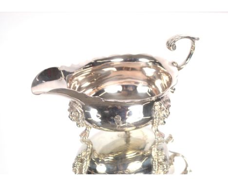 A George II silver cream jug by Joseph Saunders having serrated border, flying C scroll handle raised on three lion mask paw 