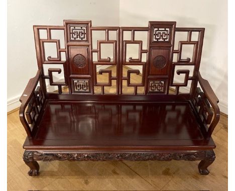 An Oriental hardwood show frame two seater sofa, having a pierced and panelled back, shaped arms and a solid seat, raised on 