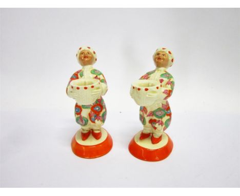 A PAIR OF CLARICE CLIFF BIZARRE WARE 'ARAB BOY' FIGURAL CANDLESTICKS, modelled as figures in turbans carrying baskets on oval