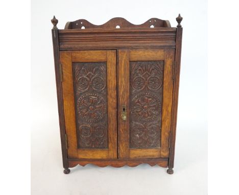 CARVED OAK SMOKERS CABINET 
with a shaped raised back above a pair of carved doors enclosing a fitted interior, with shaped s